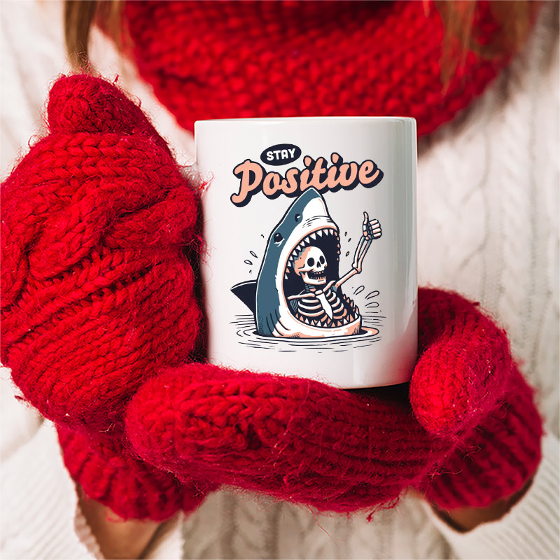 Stay Positive Funny Skeleton Shark Positivity Cup held in red mittens